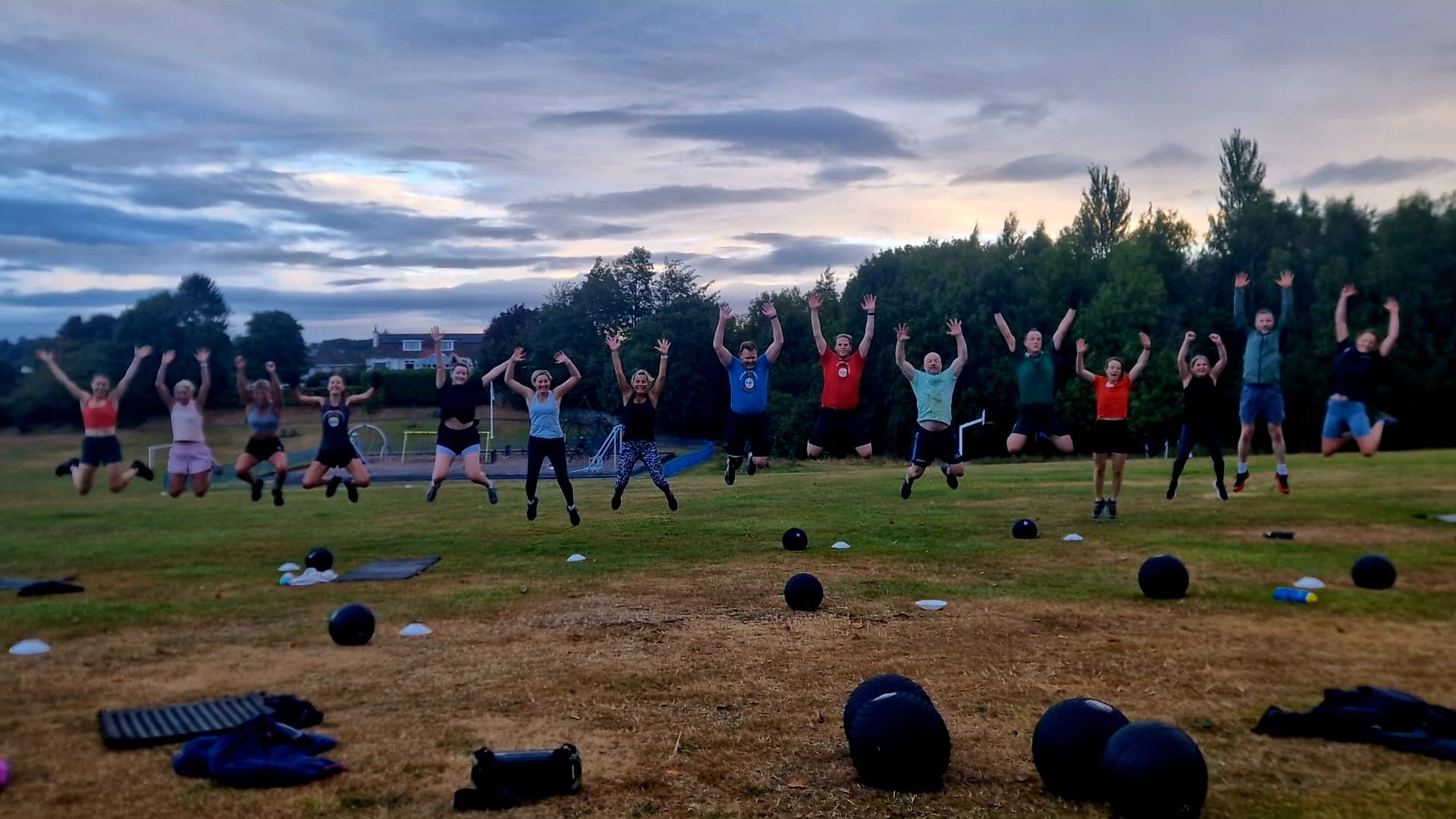 Edinburgh Bootcamp members jumping together at the end of a class in Fairmilehead Park at dusk